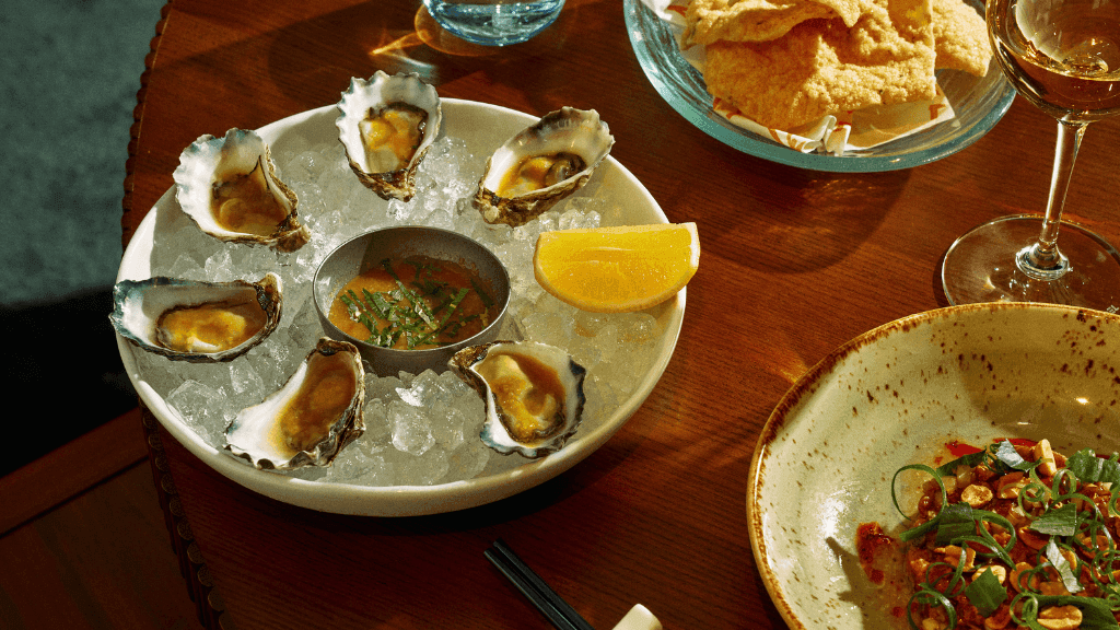 Plates of oysters, fried fish, and seafood with a wine glass on a wooden table for Easter Seafood Banquet at Delta Rue.