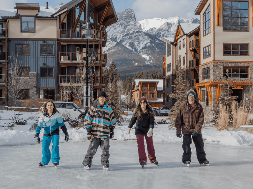 Group of friends ice skating on a frozen outdoor rink near the snowy peaks at Spring Creek Resorts, featuring Canmore events