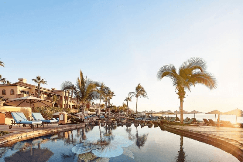 Resort pool with lounge chairs, umbrellas, and palm trees at Hotel Hacienda del Mar los Cabos