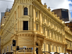 Ornate pale yellow building, the 'Old Bank Shopping Arcade', on a city street corner with a traffic light and modern buildings in the background.Ornate pale yellow building, the 'Old Bank Shopping Arcade', on a city street corner with a traffic light and 