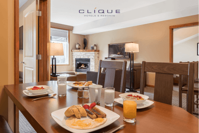 Dining table with breakfast in a suite at Falcon Crest Lodge, with a living area featuring a fireplace in the background