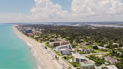 Aerial view of sandy coastline by turquoise ocean with coastal homes under cloudy skies near Star Suites Vero Beach