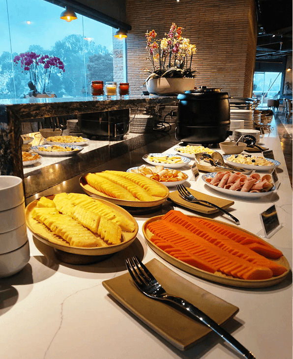 Bufé de desayuno con piña y papaya en rodajas, embutidos y orquídeas en Hotel B3 Sibelius