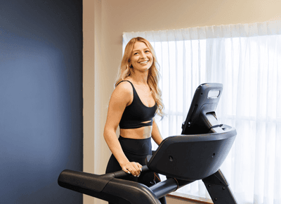 Woman exercising on a treadmill by a bright curtained window in the fitness room at Rodd Crowbush Golf & Beach Resort