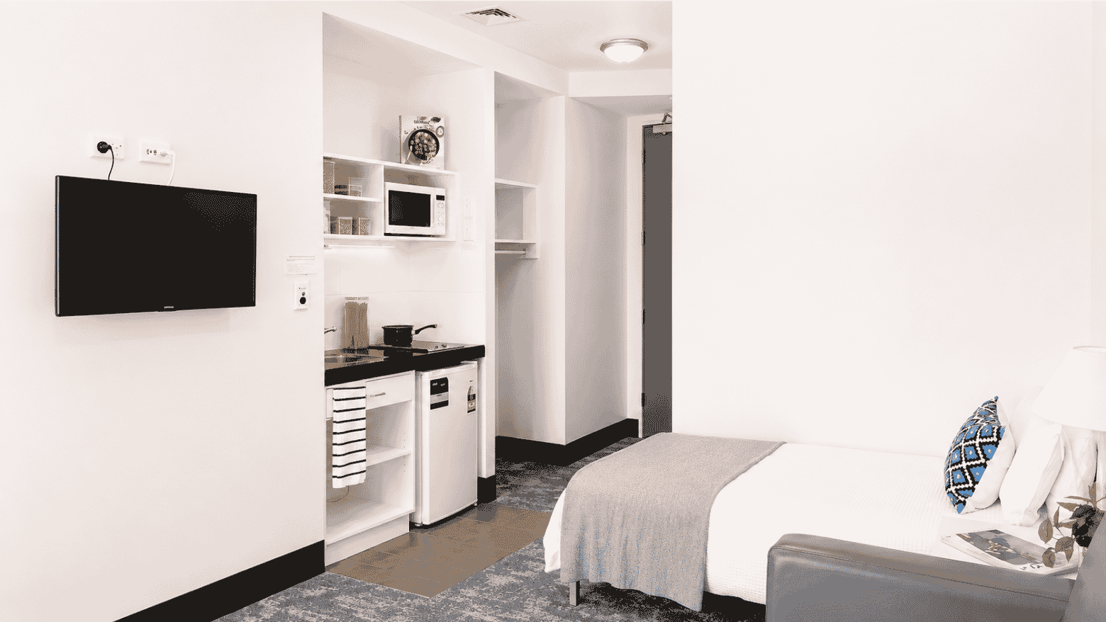 Modern studio apartment with kitchenette, wall-mounted TV, and comfortable bed at Student Living Waymouth