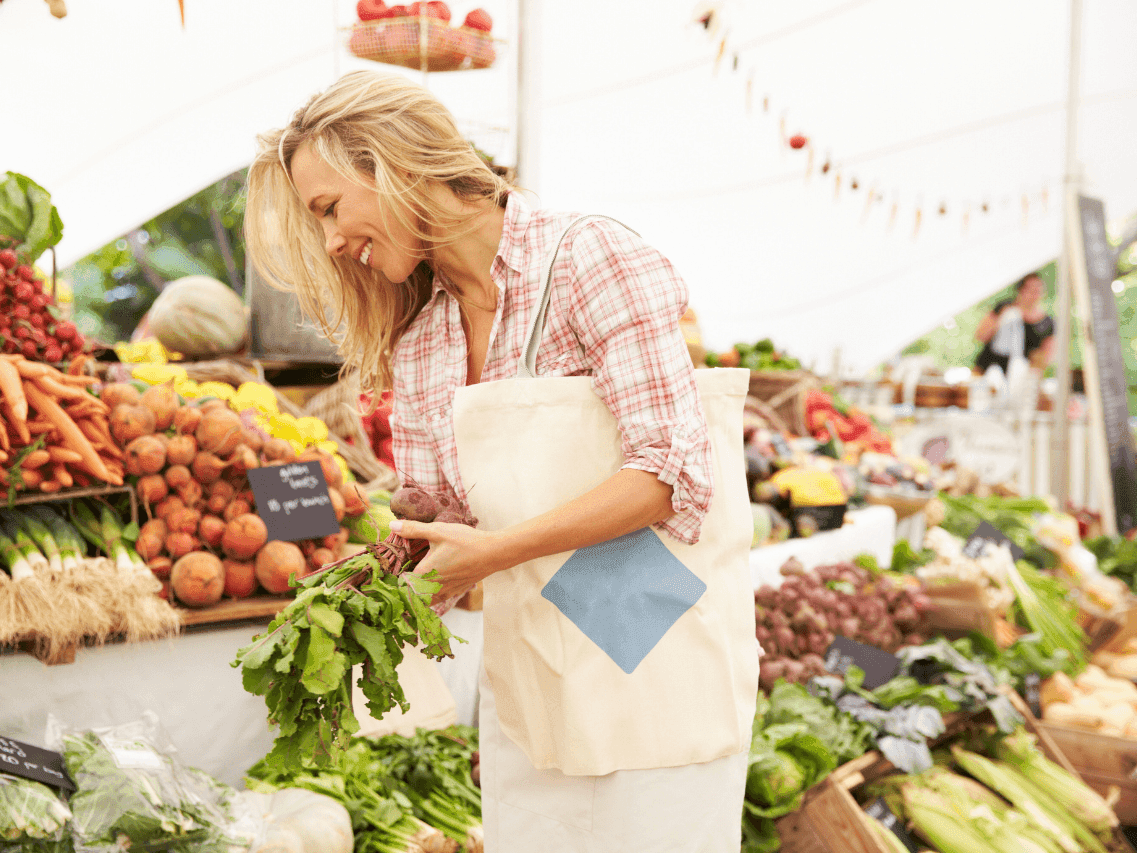 Woman gathering fresh vegetables at Harvest Market filled with colorful produce and greenery near Ogunquit Hotel & Suites