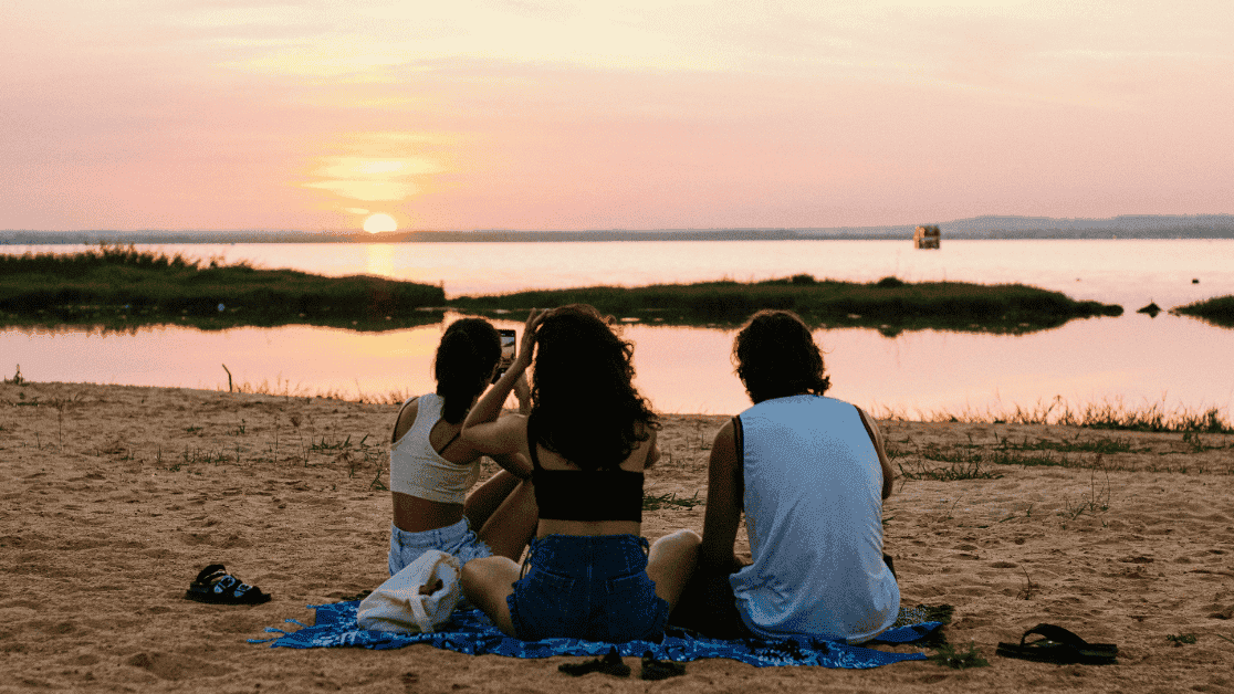 Three friends on a beach at sunset taking photos.