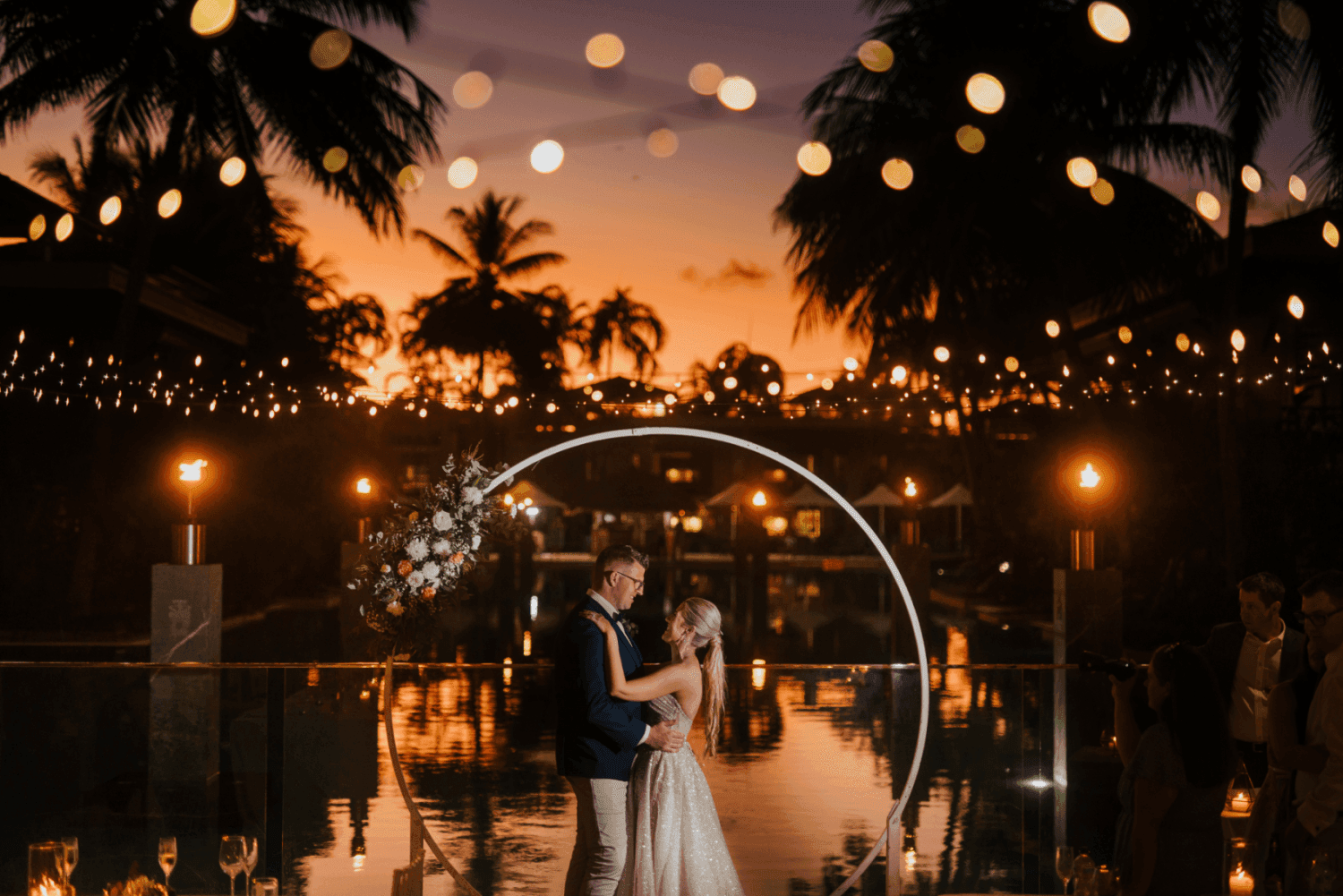 Couple embracing by pool & circular floral arch in Four Mile Beach at Pullman Port Douglas Sea Temple Resort & Spa