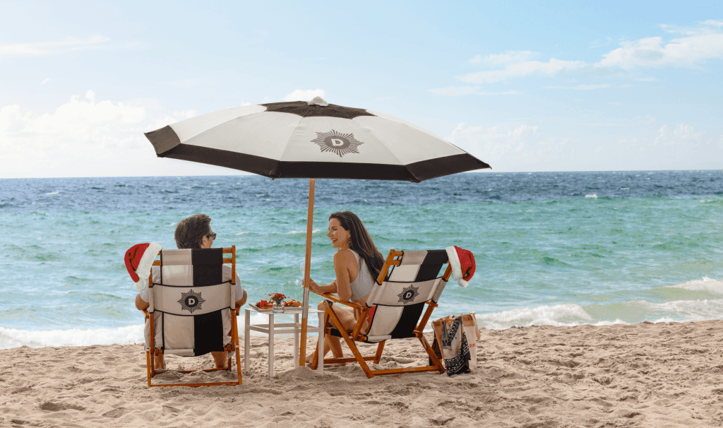 Couple relaxes on beach chairs under a striped umbrella by the ocean at The Diplomat Resort