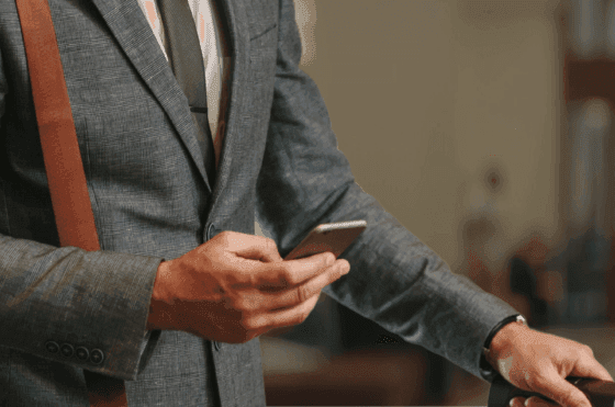 Businessman in a grey suit and tie checking his smartphone, standing near his luggage at The Grace Sydney