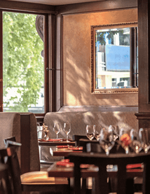 Margaux Restaurant interior featuring plush booth seating and large glass windows overlooking lush green outdoor trees