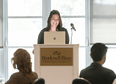 Smiling businesswoman speaking at a podium with a laptop during a corporate conference event at Rodd Brudenell River