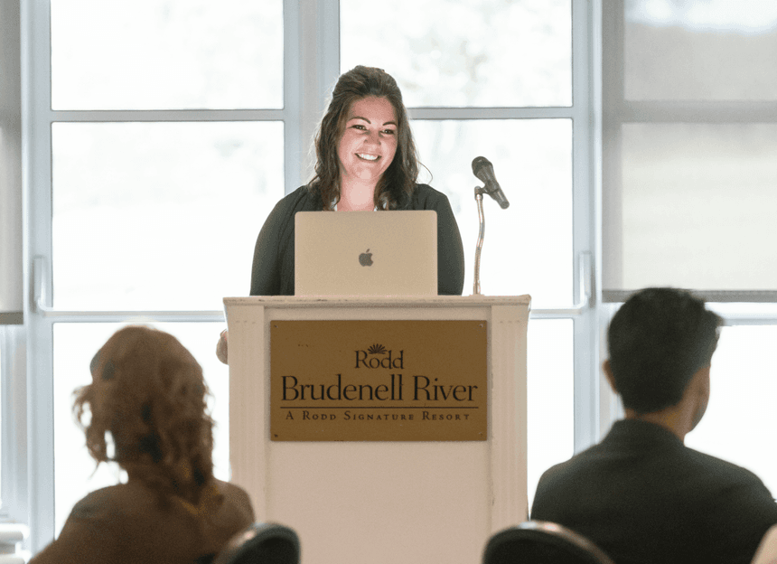 Smiling businesswoman speaking at a podium with a laptop during a corporate conference event at Rodd Brudenell River