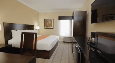 Bed with a TV and microwave by a dark wood dresser in the King Room at Galleria Palms Hotel