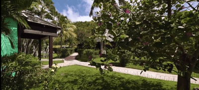 Paved garden pathway winding past tropical greenery and a wooden pavilion gazebo at Emerald Beach Resort