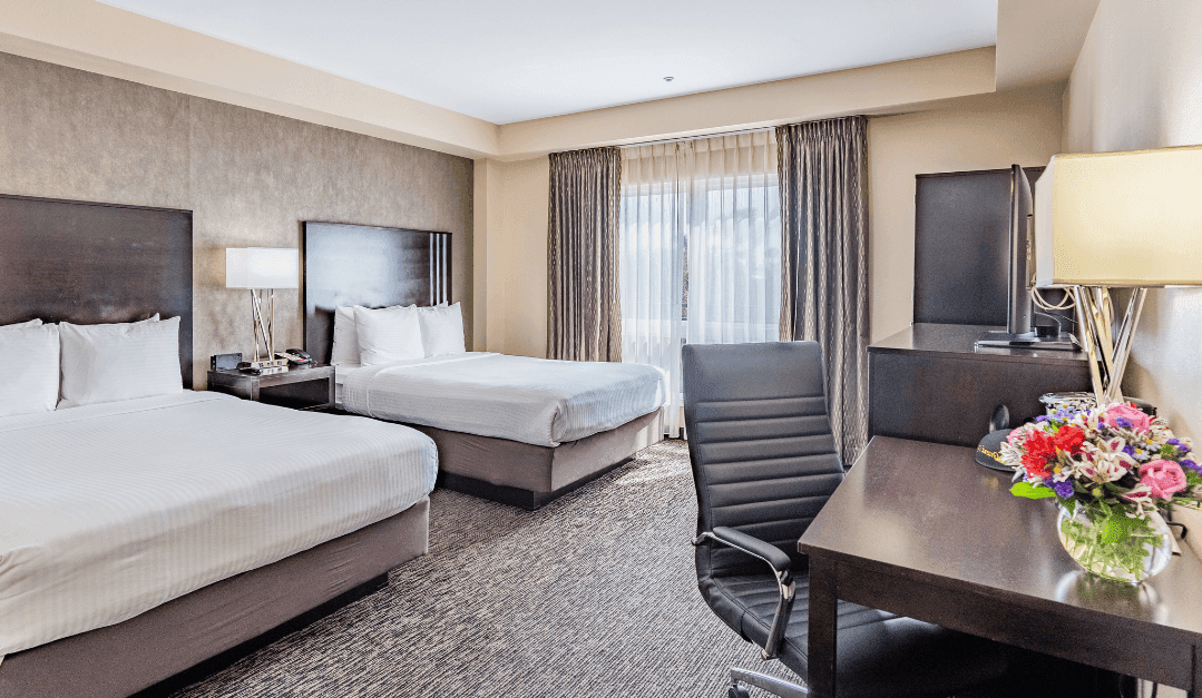 A hotel room with two double beds, a desk, chair, and TV.