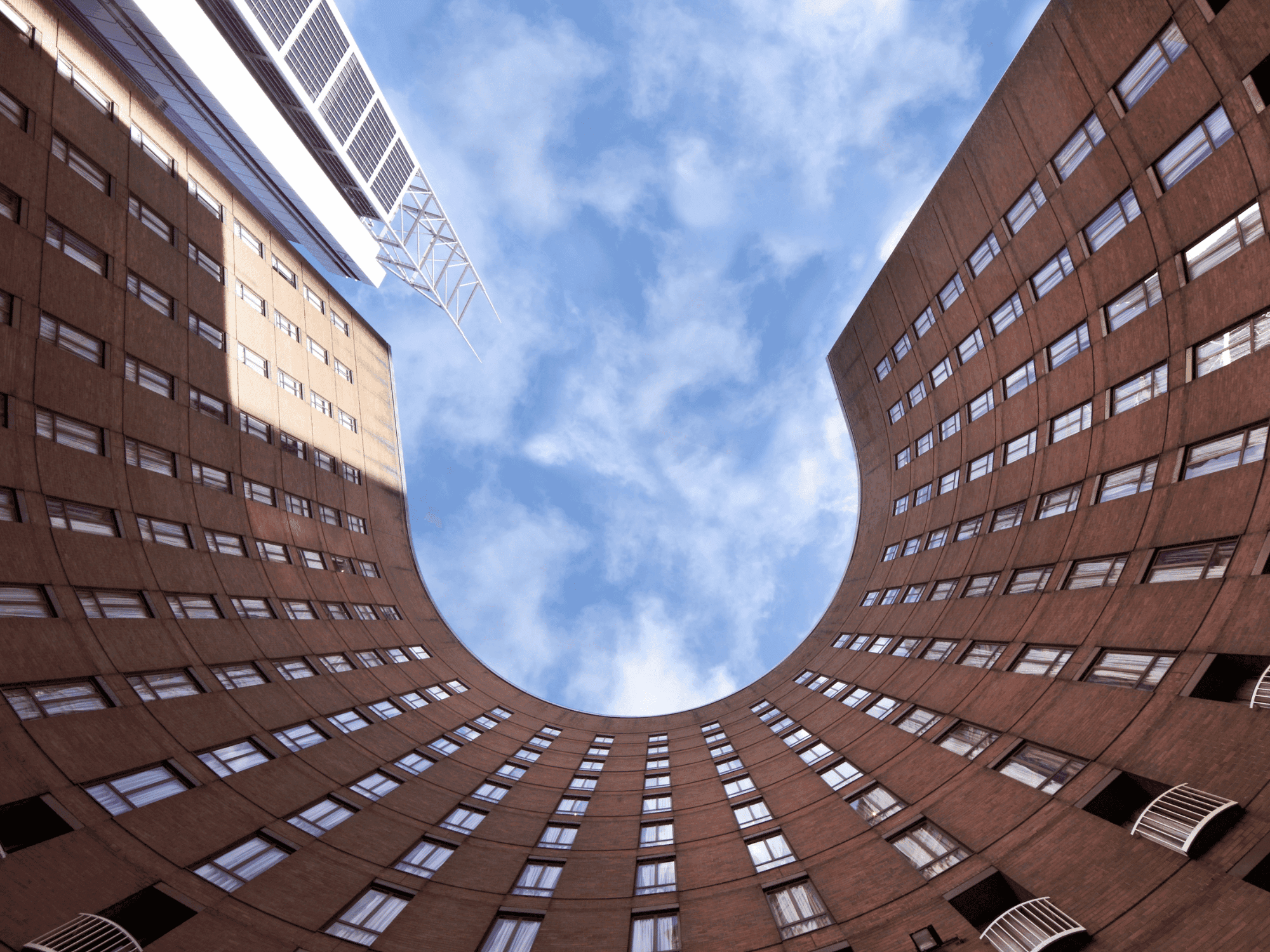 Looking up at a spiral-shaped building with many windows and a blue sky above.