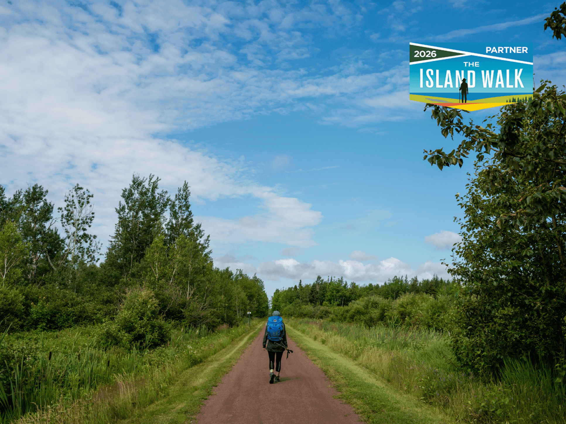 Hiker with a blue backpack walking down a red dirt trail bordered by green trees near Rodd Charlottetown Hotel