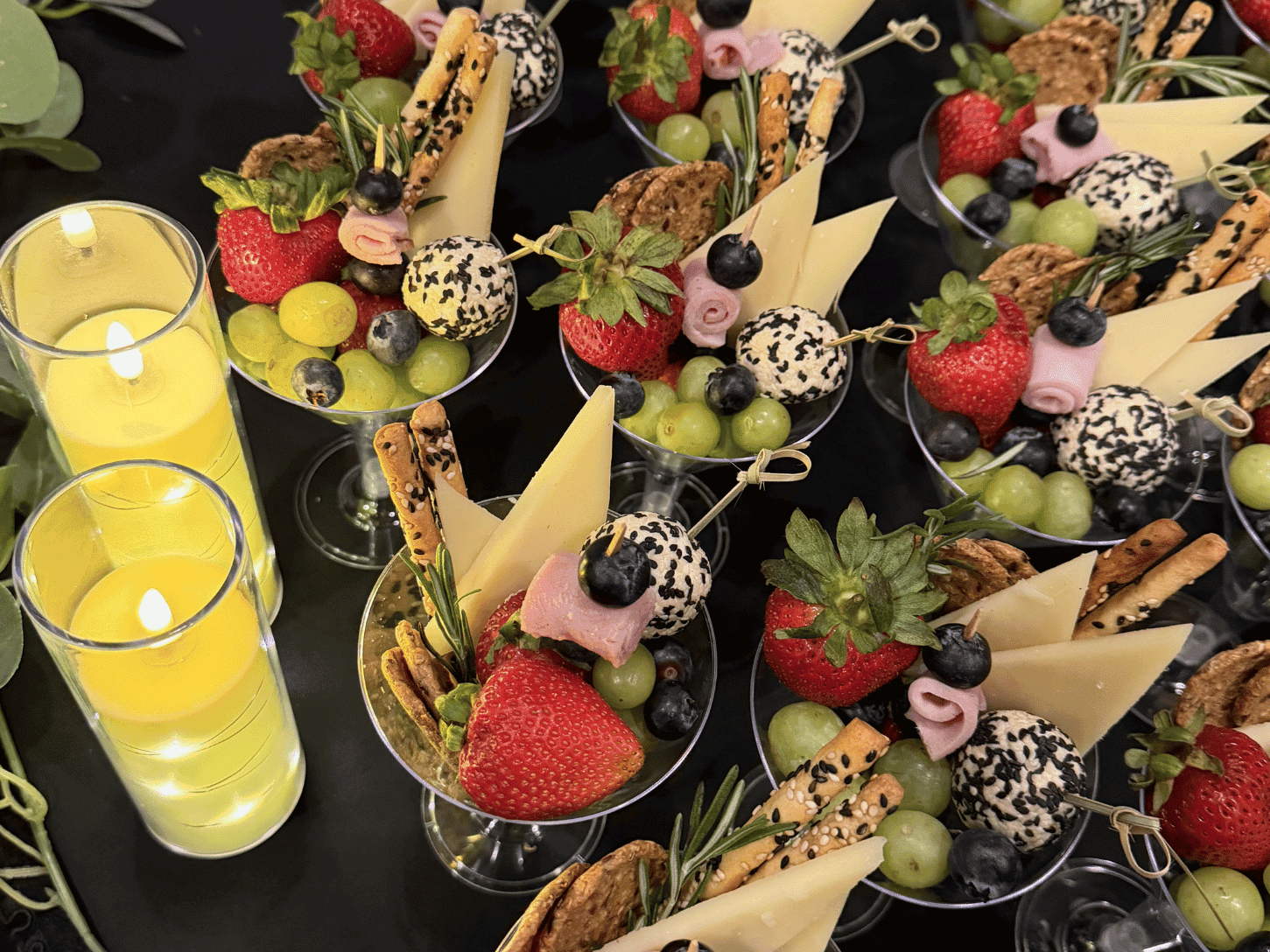 Individual charcuterie cups filled with fruits, cheeses, and crackers next to yellow candles at Rodd Grand Yarmouth