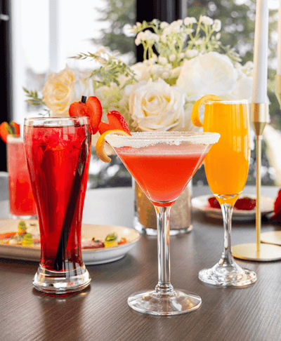 Vibrant cocktails and orange mimosa on a dining table with a floral centerpiece bouquet backdrop at Rodd Miramichi