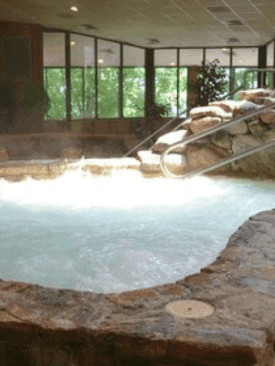 The Indoor Hot Tub with a stone wall architecture and outdoor view at Cove Pocono Resorts