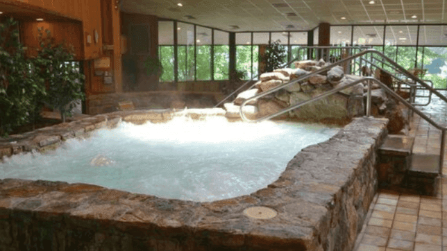 The Indoor Hot Tub with a stone wall architecture and outdoor view at Cove Pocono Resorts