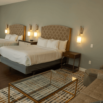 Spacious guest bedroom with two beds, lamps beside a glass-top coffee table, and seating at La Tourelle Hotel and Spa