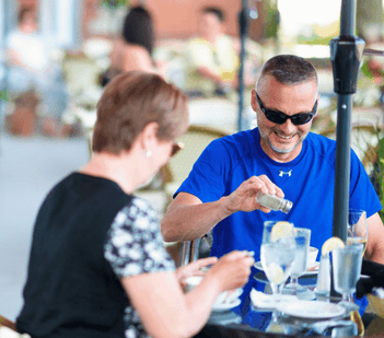 Couple dining on a patio by a glass-top table under an outdoor umbrella shade at Rodd Charlottetown Hotel