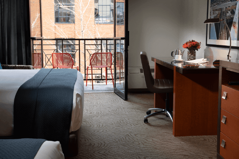 A hotel room with a queen bed, desk, and balcony access