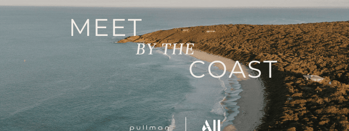 Aerial view of a sandy beach meeting calm ocean waters with rocky coastline and Meet by the Coast text overlay.