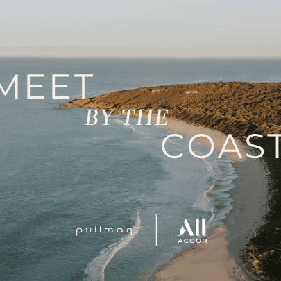 Aerial view of a sandy beach meeting calm ocean waters with rocky coastline and Meet by the Coast text overlay.
