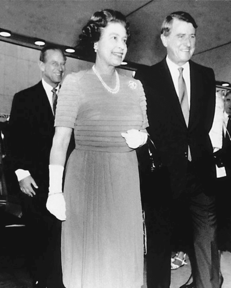 A black and white photograph of three formally dressed individuals walking in a hallway.