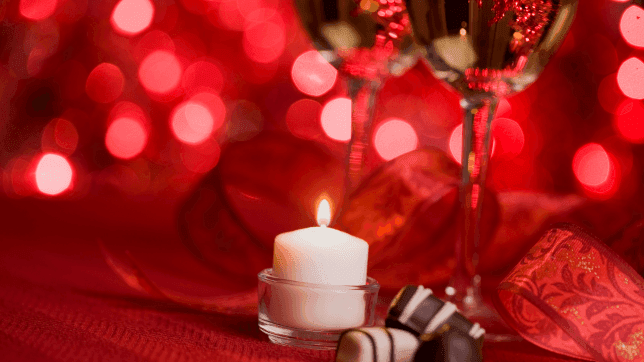 Close-up of a candle lit by a romantic dinner table arrangement, with chocolates and wine glasses at Cove Pocono Resorts
