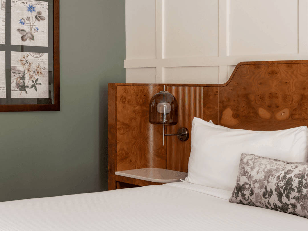 Bedroom with a wooden headboard, white bedsheets, framed wall art, and a small wall-mounted lamp.
