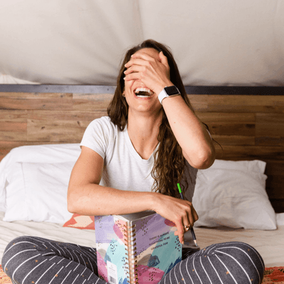 Guest laughing on bed with open journal and pencil in hand during relaxing stay at La Tourelle Hotel and Spa
