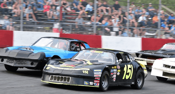 Three cars racing on a track with a crowd watching near Harrison Lake Hotel