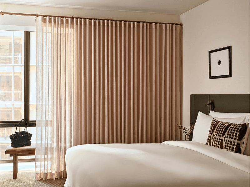 Elegantly styled hotel room with a large bed, curtains, and window showcasing The Suite Life.