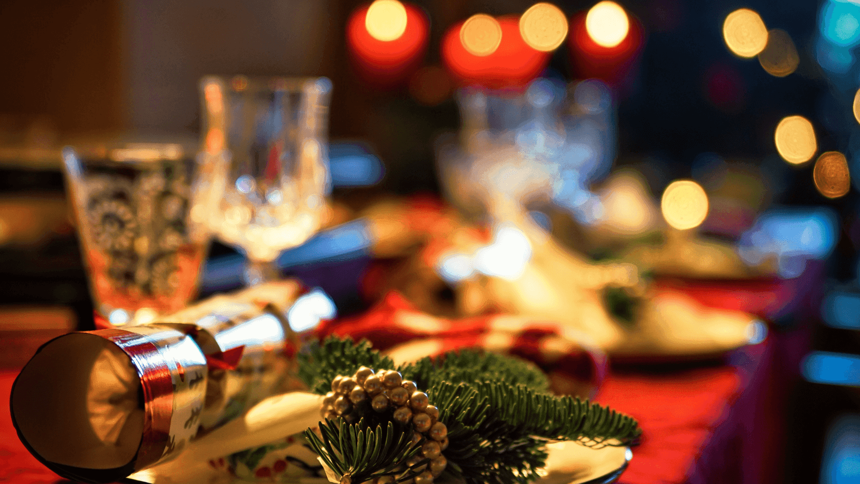 Festive table setting with a plate featuring a cracker and greenery, surrounded by candles and glassware.