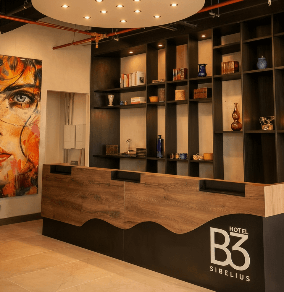 Wooden reception desk with wave base by dark shelving of vases and books, near a colorful portrait at B3 Virrey Hotel