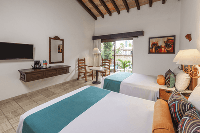 A hotel room with two beds, chairs, table, TV, coffee maker, and a balcony with a view.