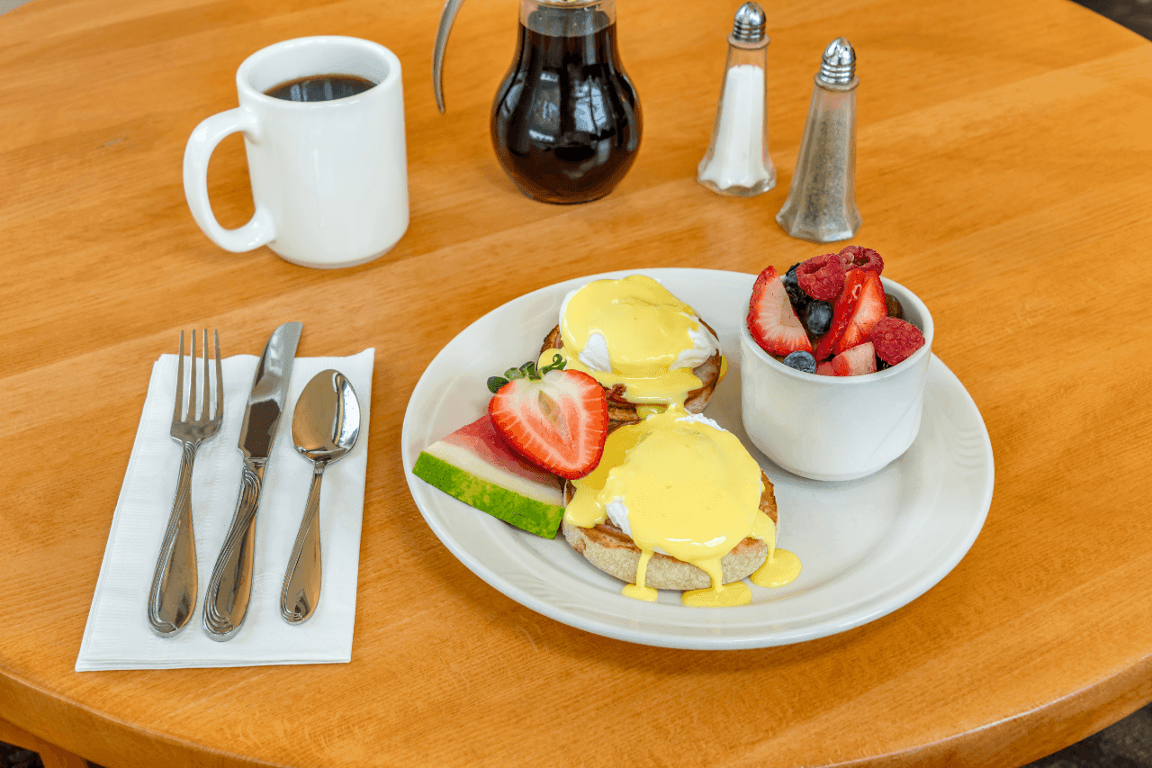 A breakfast plate with eggs benedict, fruit, and coffee