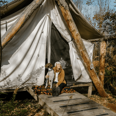 Woman sitting with dog on wooden porch outside canvas glamping tent at Firelight Camps in La Tourelle Hotel and Spa