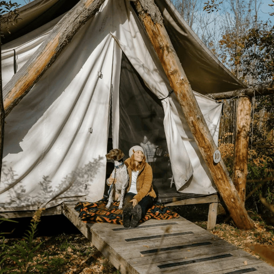 Woman sitting with dog on wooden porch outside canvas glamping tent at Firelight Camps in La Tourelle Hotel and Spa