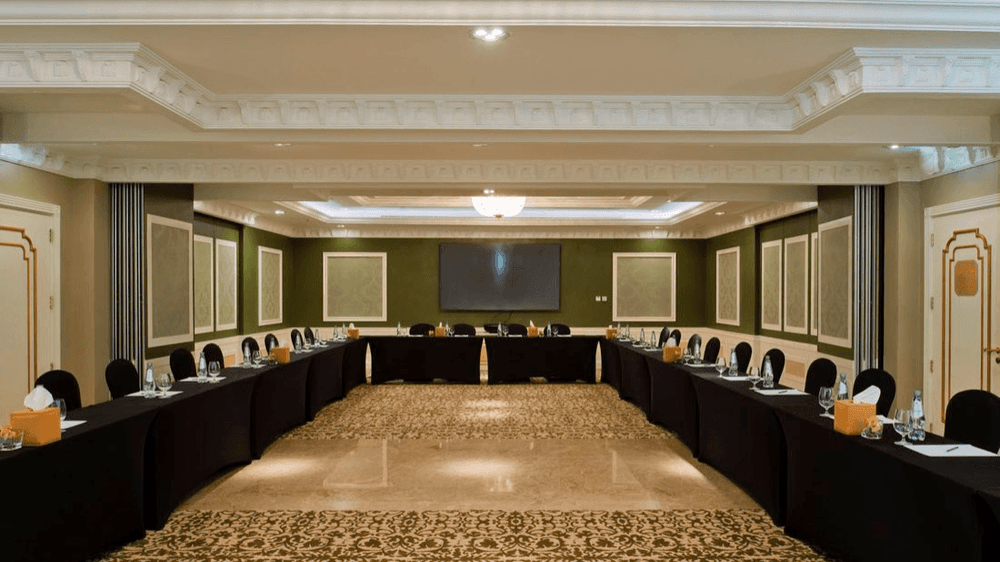 Black chairs by a U-shaped table under a large crystal chandelier in Emerald Room at Warwick Doha Hotel