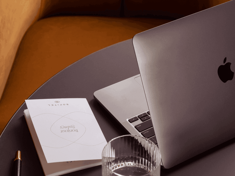 MacBook laptop open on hotel room desk with notebook and warm ambient lighting