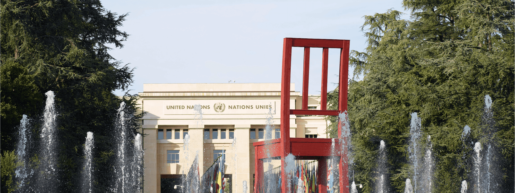 Red chair sculpture with water fountains in front of Palais des Nations building.