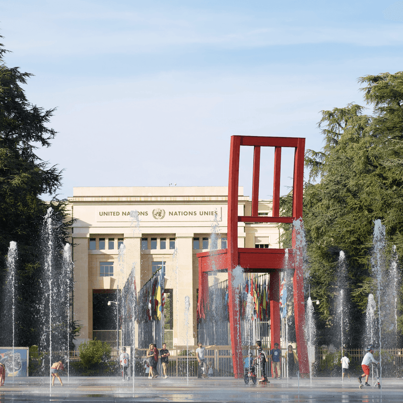 Red chair sculpture with water fountains in front of Palais des Nations building.