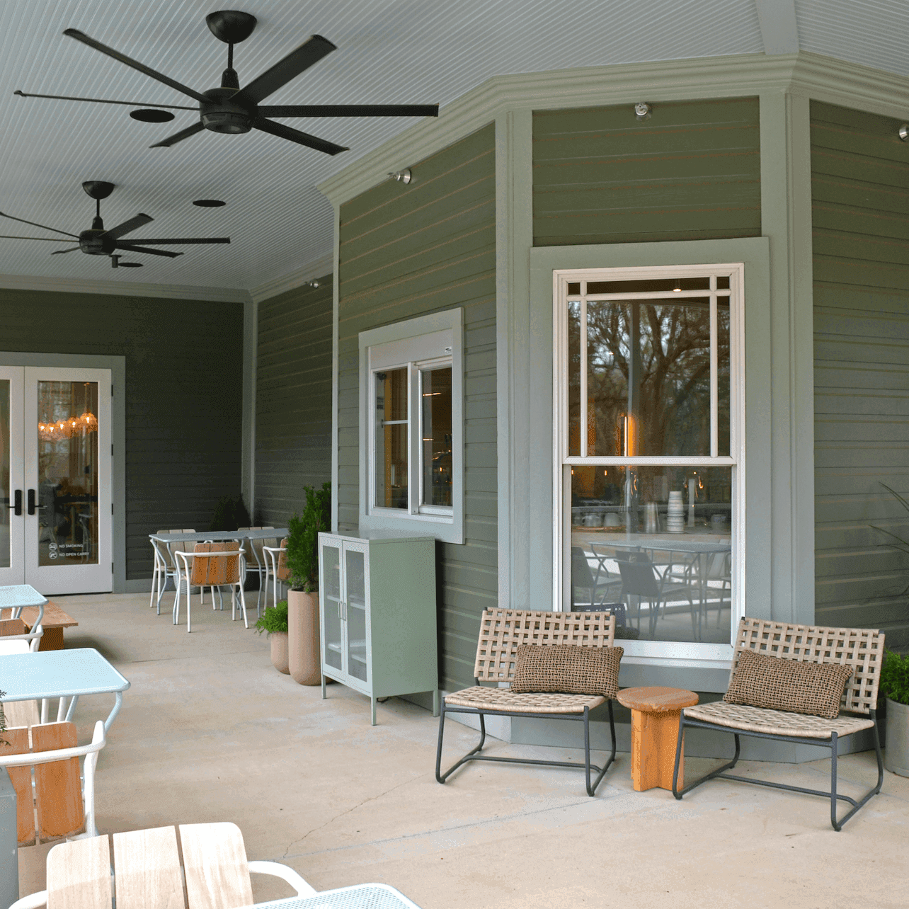 An outdoor seating area with tables, chairs, potted plants, and ceiling fans.
