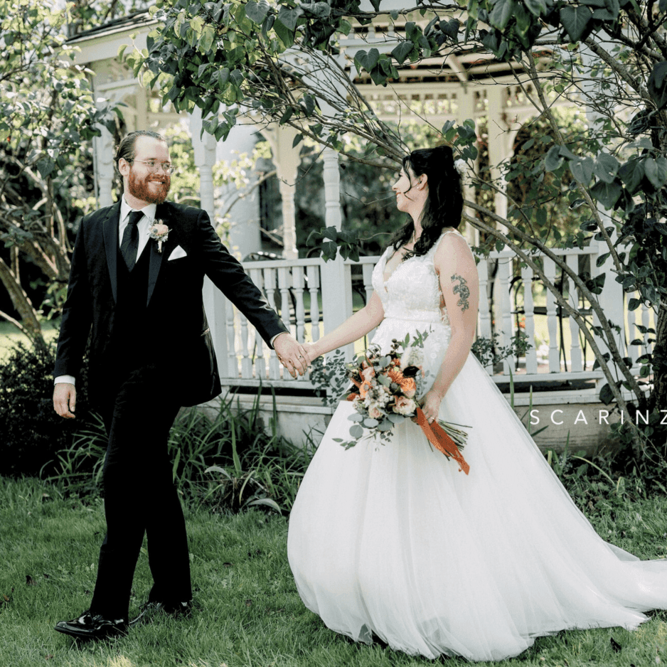 Bride and groom holding hands and walking together beside a white gazebo under leafy trees at La Tourelle Inn and Spa