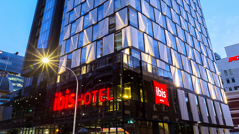 Exterior view of the Ibis Adelaide with glass facade and prominent illuminated signage